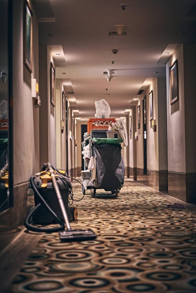Cleaner with a vacuum and cart in a long carpeted corridor